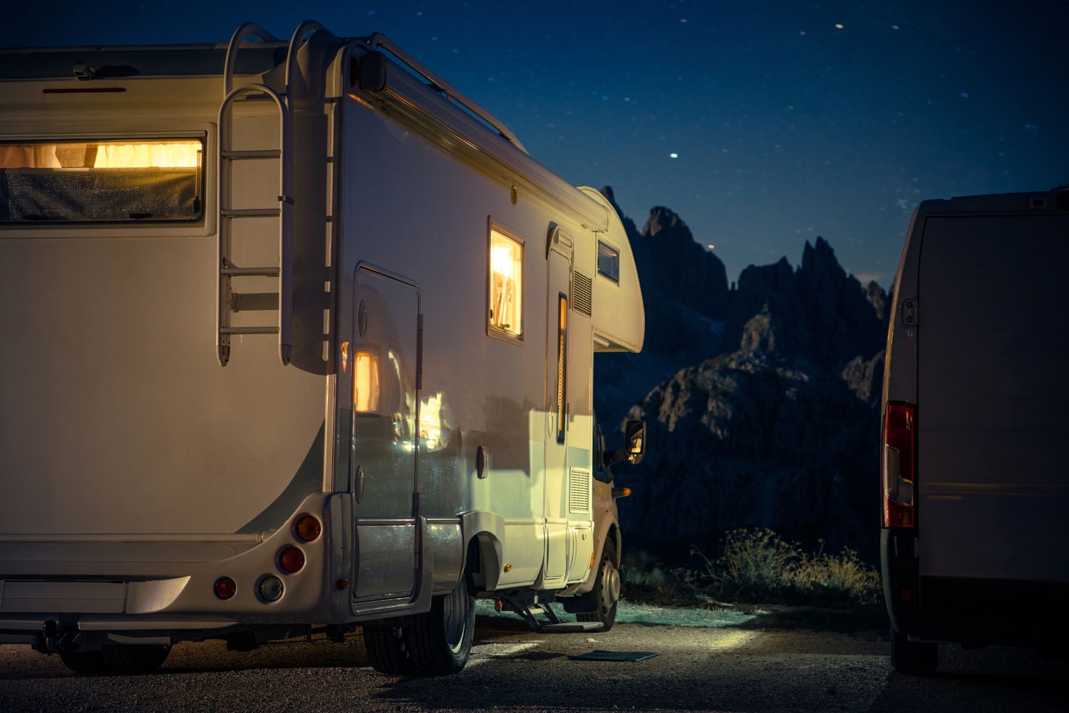 Recreational vehicle parked under a starry night sky in a serene, open area. 